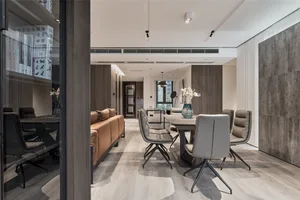 A modern residential dining room with a wooden floor, a brown leather sofa, and grey chairs. The room features contemporary d