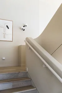 Modern staircase with wooden steps, a white handrail, and minimalist wall art featuring an abstract face with black and white