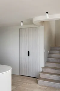 Modern home entryway featuring a white wooden cupboard with black handles and stairs leading up to another level.