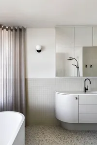 Modern bathroom featuring white terrazzo tiles, a sleek white vanity with curved edges, and a freestanding tub with a neutral
