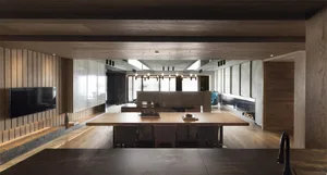Modern minimalist living room featuring dark wooden flooring, walls, and furniture, with a large table and chairs, and a warm