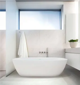 A modern minimalist bathroom with a white freestanding tub, marble walls, and a large window.