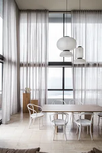 A modern residential dining room with white chairs, a wooden table, and sheer curtains allowing natural light to fill the spa