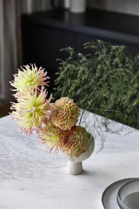 a bouquet of delicate flowers arranged in a modern vase, placed on a marble surface.