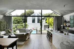 Modern living room with concrete walls and floor, large windows, and a pool in the background.