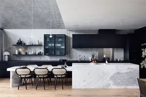 A modern minimalist kitchen featuring a white marble island, black cabinets, and concrete walls.