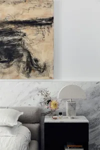 A minimalist bedroom with a marble headboard and nightstand, featuring flowers and a lamp