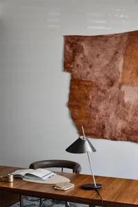 A minimalist workspace featuring a wooden desk, chair, and lamp, with a brown fabric hanging on the wall.