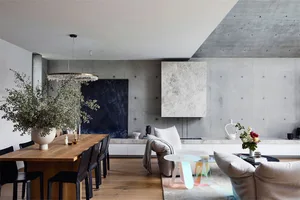A modern living room with concrete walls, a wooden dining table, and minimalist furniture.