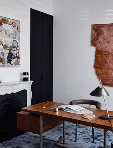 A modern study room featuring a wooden desk, leather chair, and abstract and textured wall hangings.