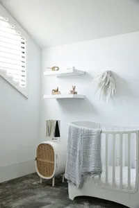A white nursery with a crib, shelves, and a white bed adorned with towels.