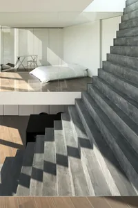 Modern bedroom with concrete stairs and a minimalist white bed.