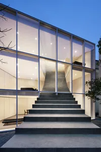 A modern house with glass walls and a concrete staircase illuminated at dusk.