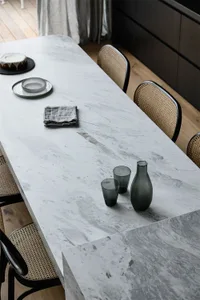 Modern kitchen interior with a marble countertop, featuring a grey cake on a plate, a gray napkin, and a set of black drinkin