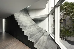 Modern architecture featuring a concrete staircase with a dark wall and glass walls overlooking green trees.