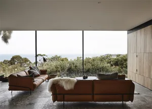 Comfortable seating area with a view of greenery, featuring leather sofas and wooden elements.