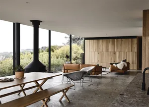 A modern living room with wood-paneled walls and a concrete floor, featuring a black fireplace, two leather sofas, a wooden d