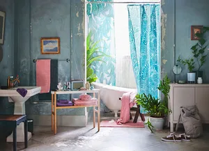 Modern bathroom with concrete walls, pink and blue accents, and tropical foliage plants.