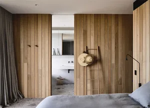 A minimalist bedroom with wood panel walls, a bed, and a bathroom with white tiles and a sink.