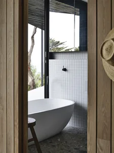 A minimalist bathroom featuring white tile walls, a porcelain bathtub, and wooden accents.