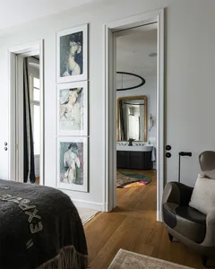 A modern bedroom featuring wooden flooring and a carpet, with a door leading to a bathroom and an armchair in the foreground.