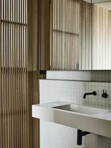Modern minimalist bathroom featuring a wood vanity and porcelain tiles, with a sleek white sink and black fixtures.
