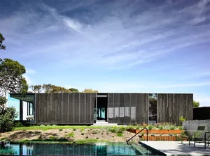 A modern house with wooden exterior walls and a large pool in the foreground.