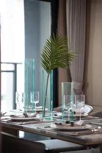 Modern table setting featuring glass vases and a green plant centerpiece on a dining table.