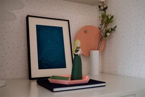 A modern home decor scene featuring minimalist artwork, a figurine, and a vase on a shelf.