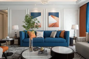 A living room with a blue upholstered sofa, decorative pillows, a round glass coffee table, and framed abstract art on the wa