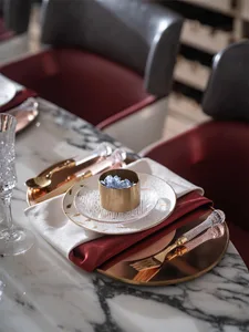 A luxurious table setting with metallic cutlery and plates, white porcelain, and a gold cup filled with blue flowers.