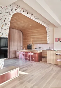 A modern kitchen featuring a wooden floor, cabinets, and island with pink stools.