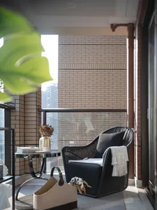 Modern residential balcony with black rattan chair, black coffee table, and green foliage.