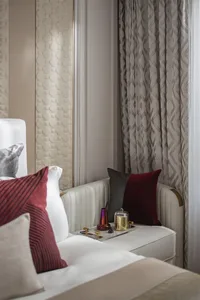 A modern bedroom featuring a bed with a white textured headboard, red and black pillows, and a nightstand with decorative ite