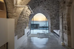A minimalist living space featuring stone walls, concrete flooring, and glass doors leading to an ocean view.