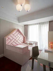 A minimalist bedroom featuring a pink bed with a woven headboard, a grey desk, and a window with sheer curtains.