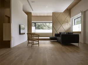 Modern interior space featuring wood flooring, minimalistic furniture, and large windows overlooking a natural landscape.