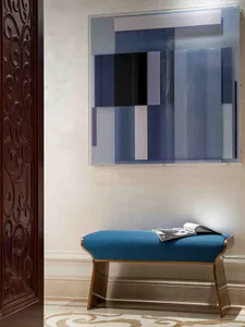 A modern interior lobby featuring a blue fabric bench with a metal frame, against a wall with a geometric art installation.