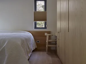 Wooden furniture and white bedding in a minimalist bedroom setting with a small window.