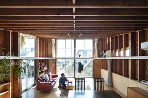 L-shaped wooden living room with a sofa and chairs, large windows, and exposed wooden beams on the ceiling.