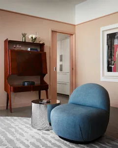 A modern living room featuring a blue upholstered chair, a wooden cabinet, and a silver cylindrical table with a textured sur