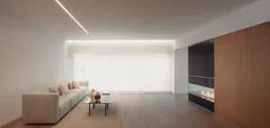 A modern minimalist living room with a long beige sofa, a glass coffee table with golden vases, and a floor-to-ceiling glass 