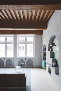 A minimalist living room with concrete walls and wooden ceiling beams.