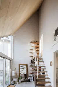 Modern minimalist interior with a wooden staircase leading up to a white brick wall, large windows letting in natural light, 