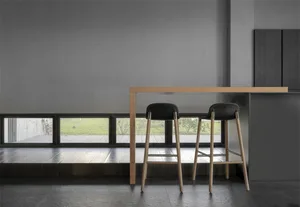 Minimalist kitchen area with wood bar table, concrete flooring, and matte black stools.