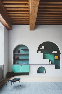 A minimalist living room with white walls, green shelves, and concrete and wooden furniture.