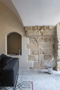 A modern minimalist living room with concrete walls and a stone accent wall, featuring a sleek black sofa and a transparent l
