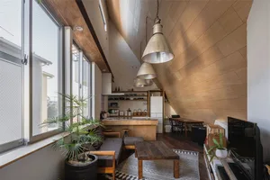 A minimalist living room and kitchen with wooden furnishings, a large window, and industrial lighting.