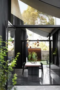 A modern dining room featuring concrete folding doors, a wooden dining table, and a unique pendant light hanging from the cei