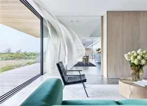 A modern minimalist residential interior with a glass wall overlooking a natural landscape.